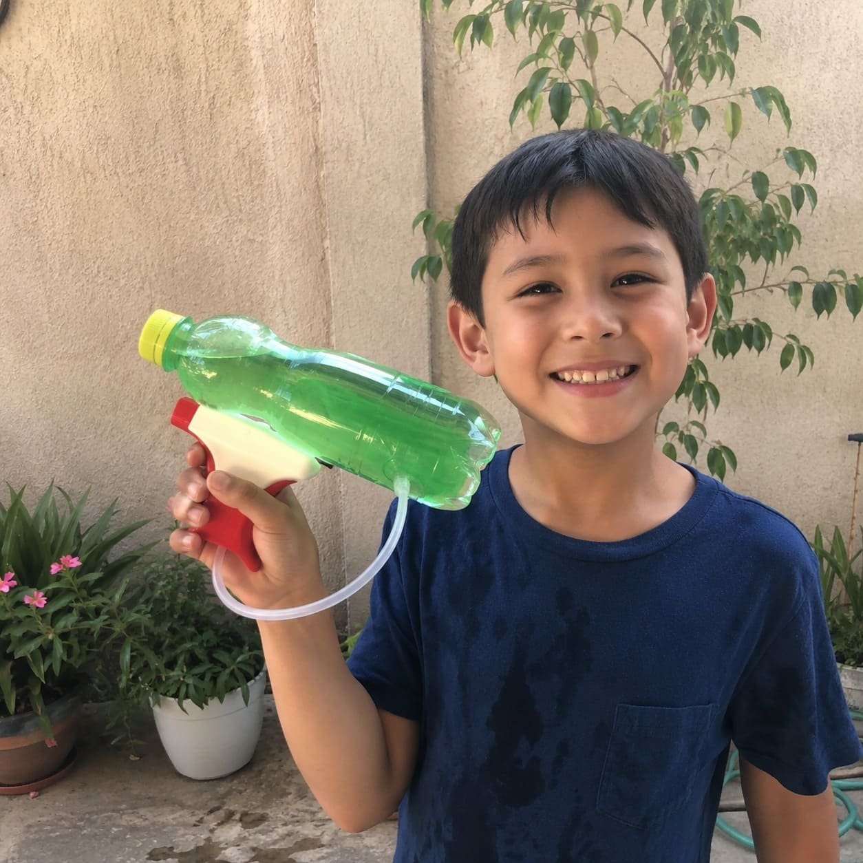 Menino feliz segurando uma arma de água feita com garrafa PET verde